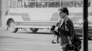 Una fotografía borrosa, sacada de un documental sobre Rodrigo y otros fotógrafos chilenos en dictadura. Rodrigo, cámara en mano, y con un bolso a cuestas, retrata las protestas de Chile en 1986.