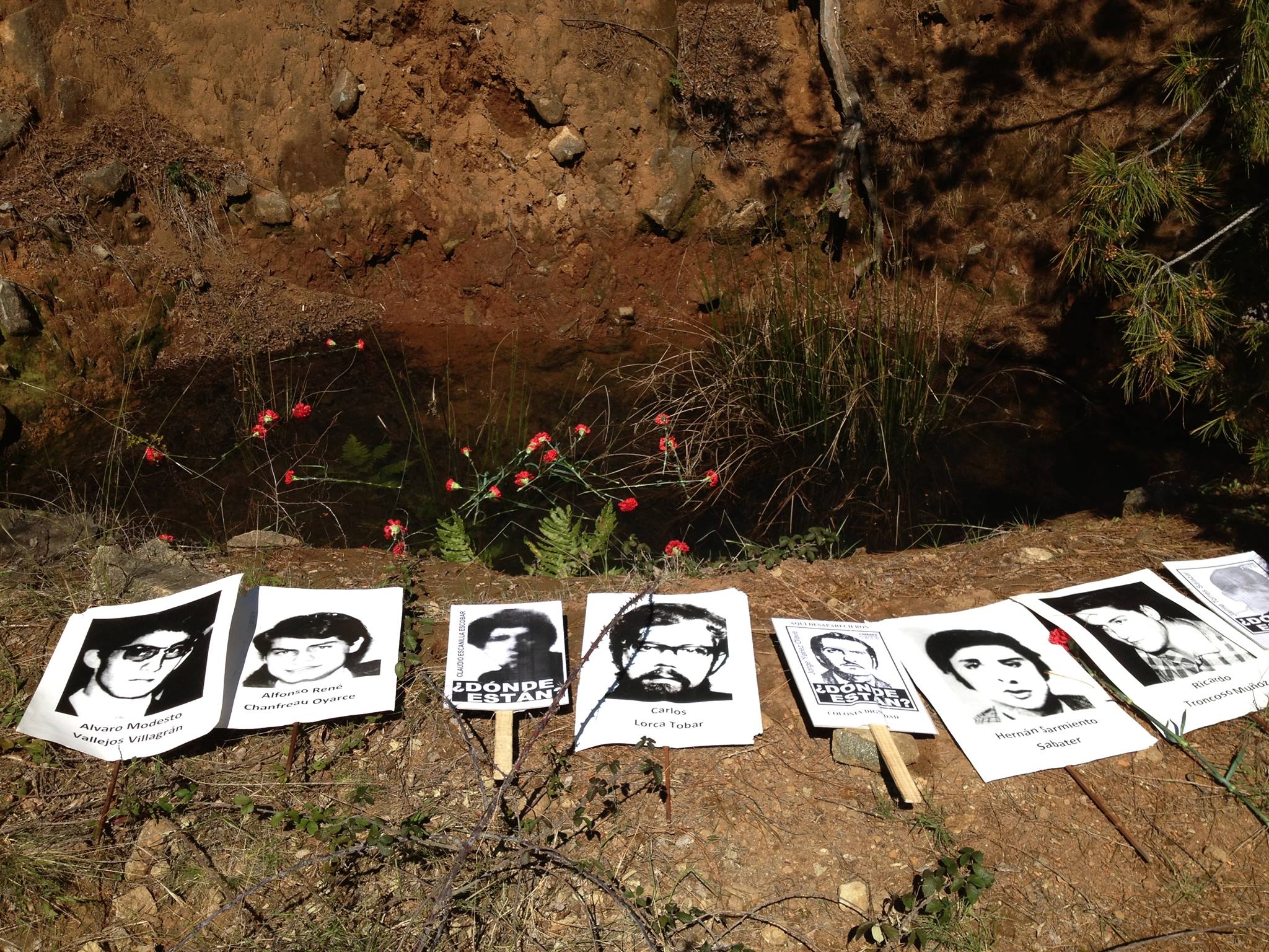 Se aprecia una zanja en la tierra. Al borde de la excavación hay fotos de detenidos desaparecidos.