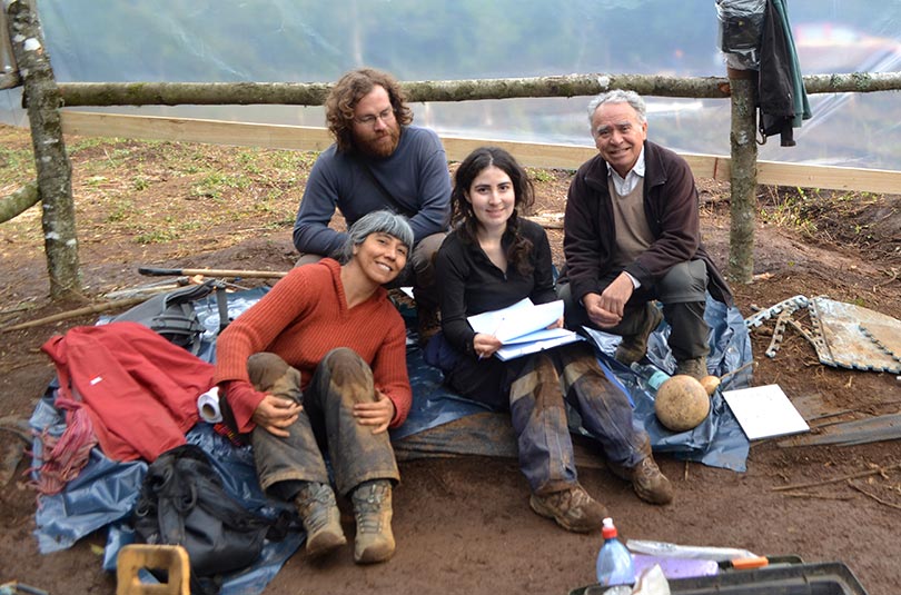 El arqueólo Iván Cáceres está sentado en el suelo junto a dos mujeres y un hombre. Tienen la ropa sucia con barro porque están en un sitio de excavación.